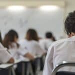 school background back view university students writing answer doing exam in classroom